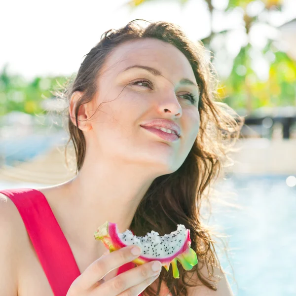 スイミング プールで座っているとドラゴン フルーツを食べる女性 — ストック写真