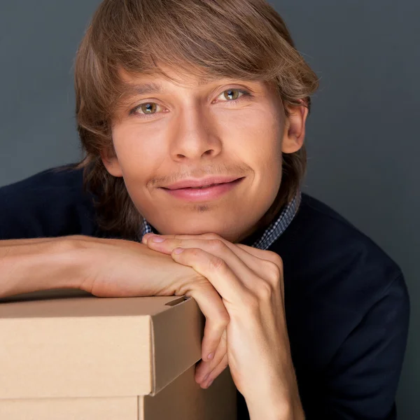 Portrait of young man leaning on box against grey wall. He is st — Stock Photo, Image