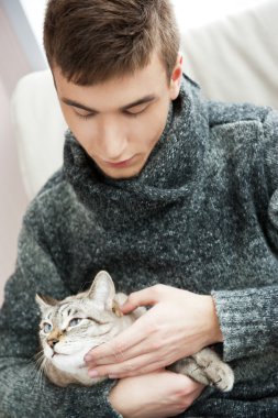 Relaxed man sitting on armchair holding and petting pet cat clipart