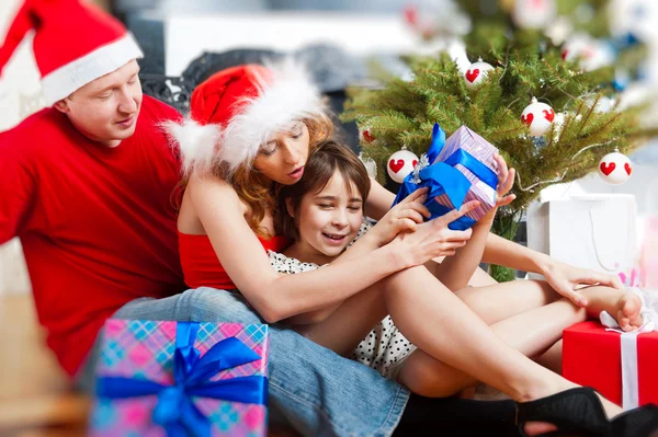 Jeune famille heureuse près d'un arbre de Noël à la maison tenant cadeau d'un — Photo