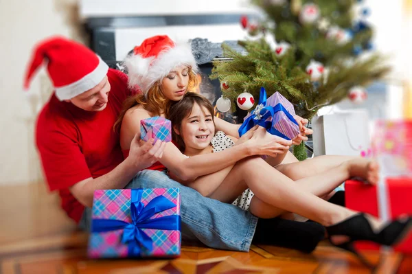 Joven familia feliz cerca de un árbol de Navidad en casa sosteniendo un regalo —  Fotos de Stock