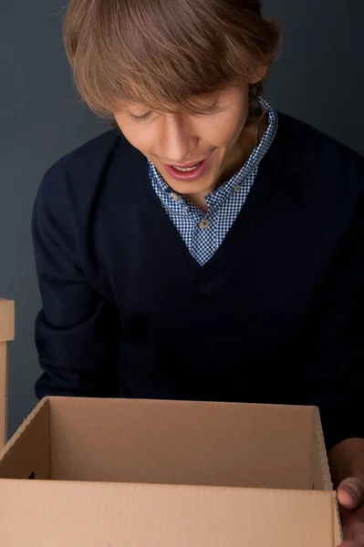 Retrato de un joven sosteniéndose en una caja contra una pared gris. Él es st —  Fotos de Stock