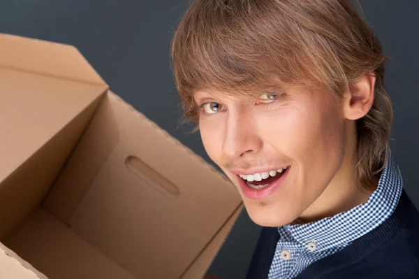 Portrait of young man holding on box against grey wall. He is st — Stock Photo, Image