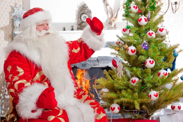 Papai Noel sentado na árvore de Natal, perto da lareira e olhando — Fotografia de Stock