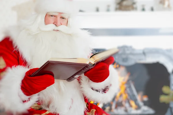 圣诞老人坐在圣诞树，靠近壁炉和阅读 — 图库照片