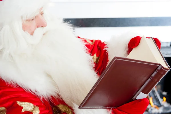 Santa sitting at the Christmas tree, near fireplace and reading — Stock Photo, Image