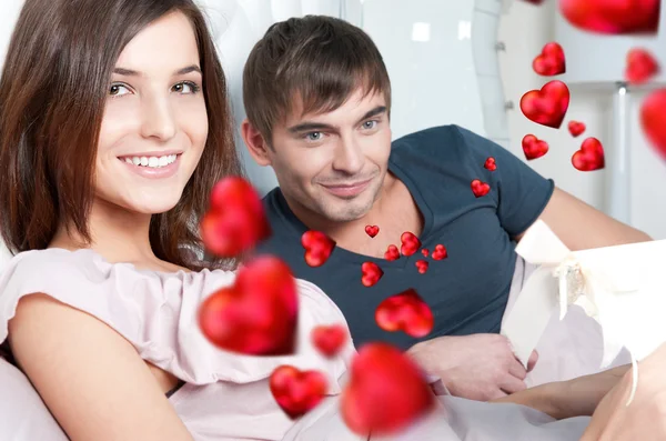Glada unga par avkopplande på sängen. man att göra en present till sin flickvän — Stockfoto