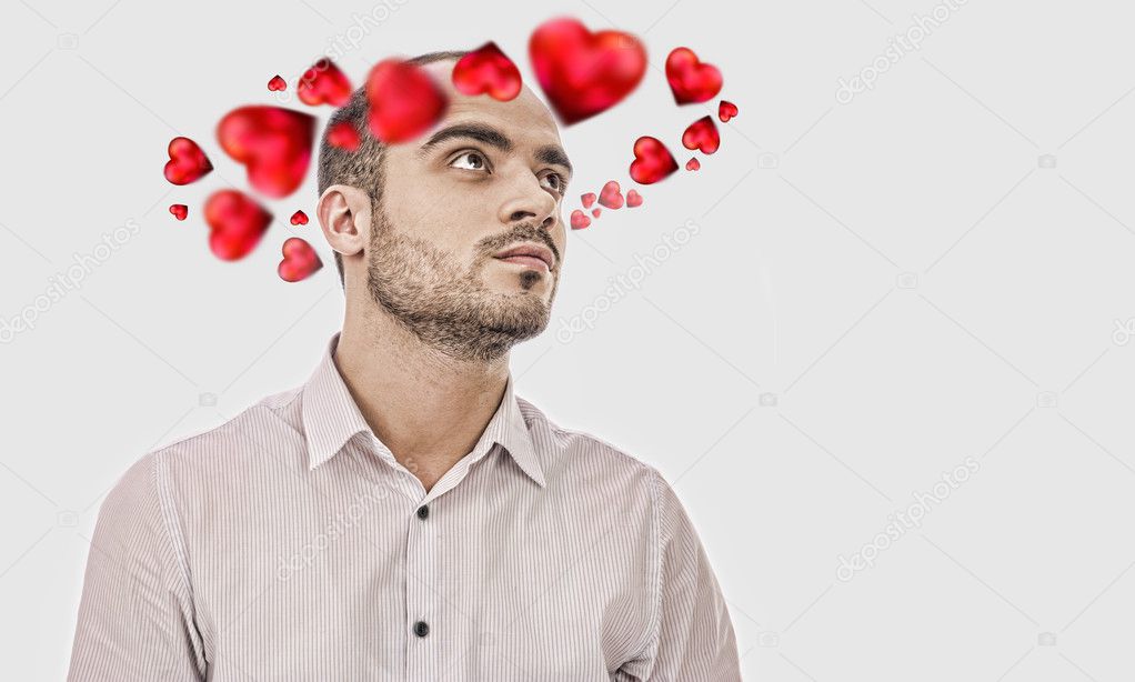 Young man thinking about love. Red hearts are flying around his