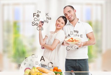 Playful young couple in their kitchen preparing healthy food and clipart