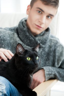 Relaxed man sitting on armchair holding and petting pet cat clipart