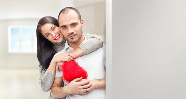 Retrato de jovem casal com coração vermelho em pé em sua casa — Fotografia de Stock