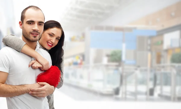 Retrato de jovem casal com coração vermelho em pé no shopping mal — Fotografia de Stock