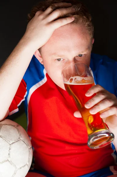 Young man holding soccer ball and beer and watching tv translati — Stock Photo, Image