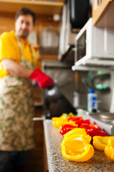 Schöner Mann, der zu Hause in der Küche kocht. Mann im Hintergrund. — Stockfoto