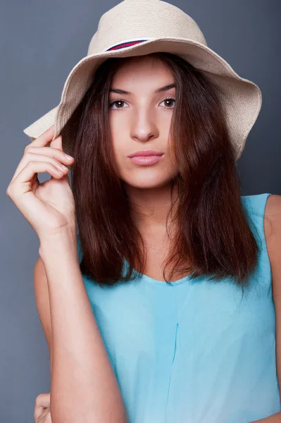 Donna fiduciosa con le braccia vicino alla testa che tiene il cappello contro un bl — Foto Stock