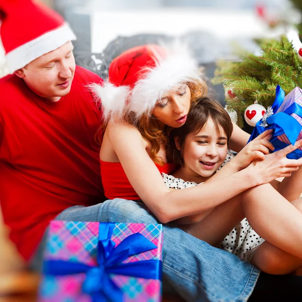 Jovem família feliz perto de uma árvore de Natal em casa segurando presente um — Fotografia de Stock