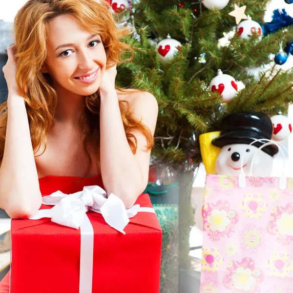 Χριστούγεννα γυναίκα κοντά ένα χριστουγεννιάτικο δέντρο που κατέχουν μεγάλο δώρο κουτί, ενώ — Φωτογραφία Αρχείου