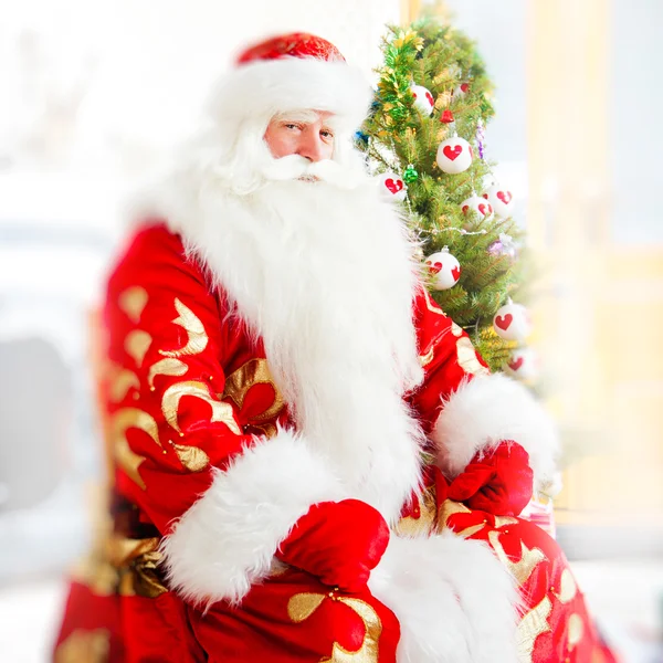 Santa sentado en el árbol de Navidad, cerca de la chimenea y mirando — Foto de Stock