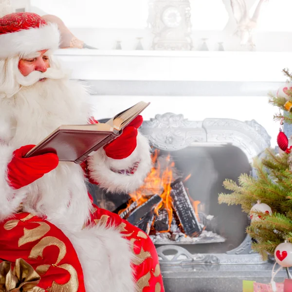 Santa ül a karácsonyfa közelében kandalló és olvasás — Stock Fotó