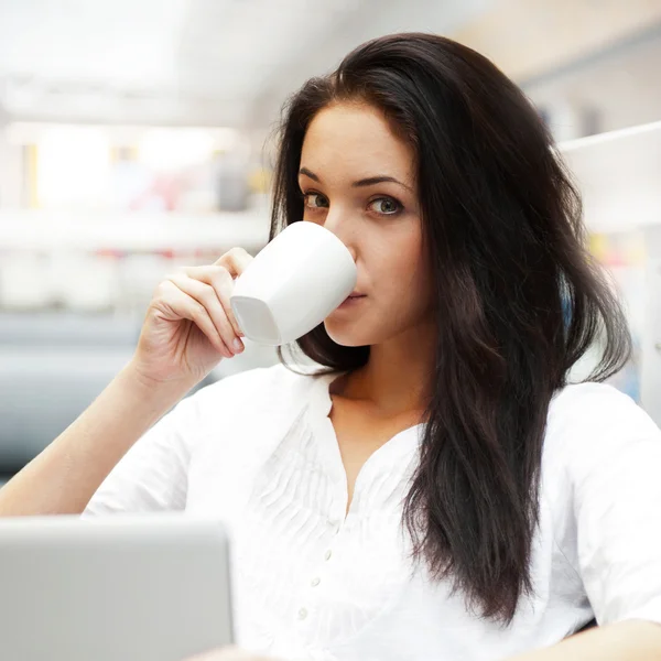 Portrait of a beautiful young woman working on laptop and drinki — Stock Photo, Image