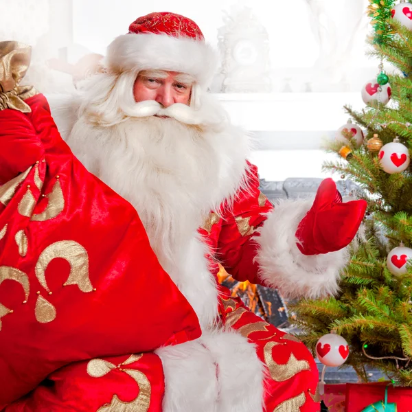Santa ül a karácsonyfa közelében kandalló és keres — Stock Fotó