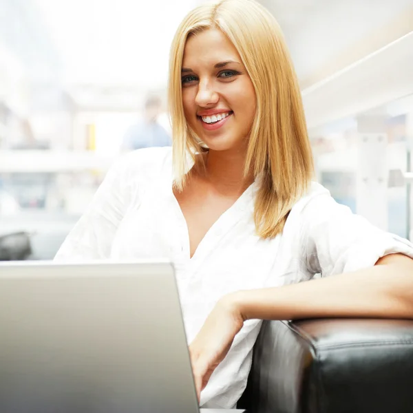 Portret van gelukkig blonde vrouw met laptop in shopping mall café — Stockfoto