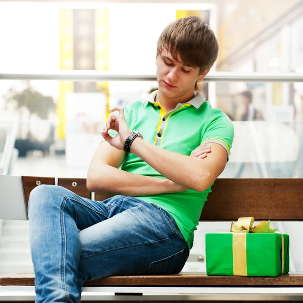 Retrato de jovem dentro shopping center com caixa de presente sentado — Fotografia de Stock