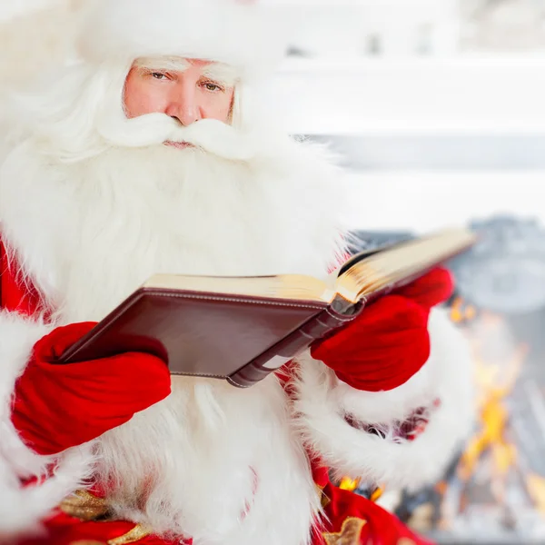 Papá Noel sentado en casa y leyendo un libro. En interiores —  Fotos de Stock