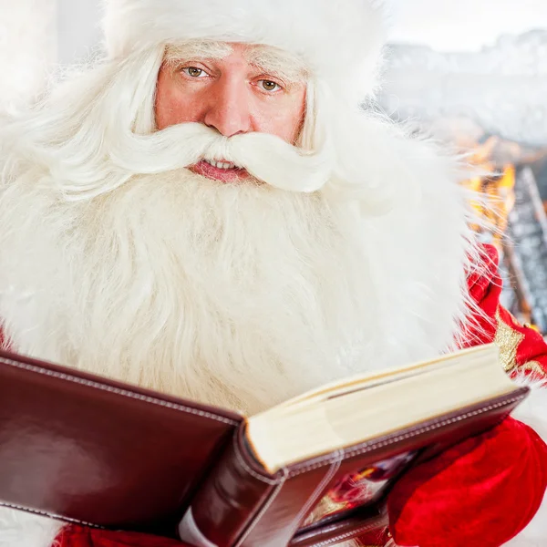 Papá Noel sentado en casa y leyendo un libro. En interiores — Foto de Stock
