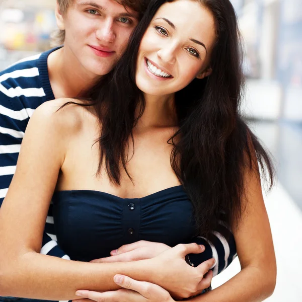 Retrato de jovem casal abraçando no shopping center e olhando — Fotografia de Stock