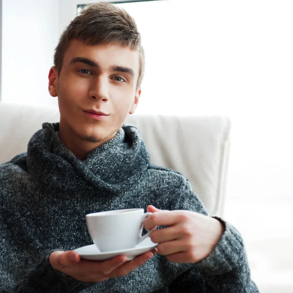 Portrait of a young man drinking coffee while sitting on armchai — Stock Photo, Image
