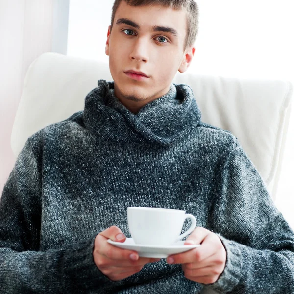 Portret van een jonge man drinken koffie zittend op armchai — Stockfoto