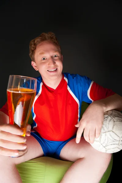 Young man holding soccer ball and beer and watching tv translation Stock Picture