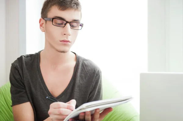Junger erwachsener Mann schreibt in sein Copybook, während er auf einem großen Stockfoto