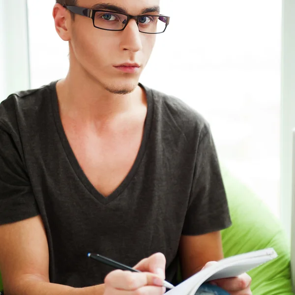 Junger erwachsener Mann schreibt in sein Copybook, während er auf einem großen lizenzfreie Stockbilder