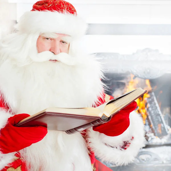 Santa sitting at the Christmas tree, near fireplace and reading Royalty Free Stock Images