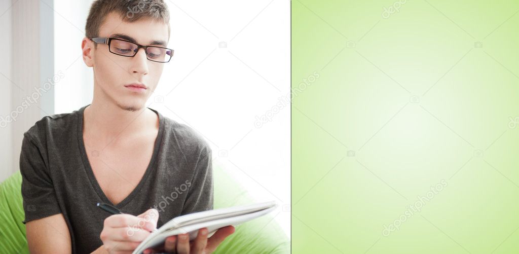 Young adult man writing in his copybook while sitting on a large beanbag at his home. Blank copyspace for your text and logo