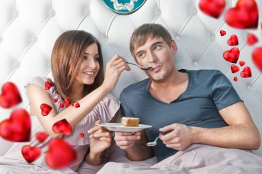 Portrait of happy couple lying in the bed. Girl feeding her boyf clipart