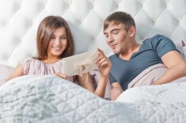 Jeune couple heureux présentant cadeau au lit — Photo