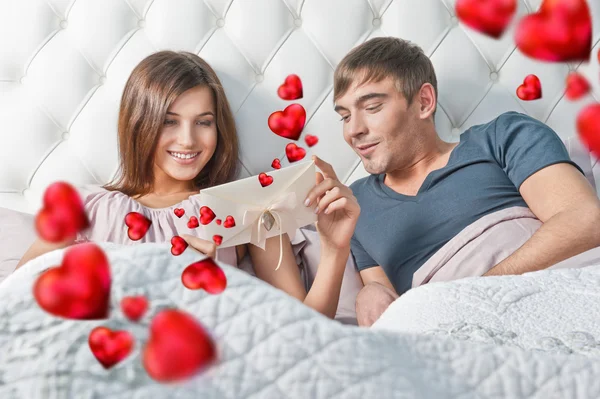 Jonge gelukkige paar presenteren geschenk in bed — Stockfoto