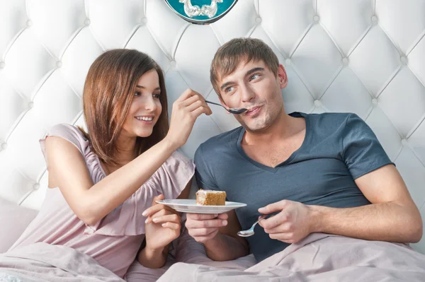 Junges munteres Paar isst Kuchen im Bett — Stockfoto