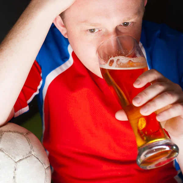 Mladý muž, držící míč fotbal a pivo a sledování tv translati — Stock fotografie