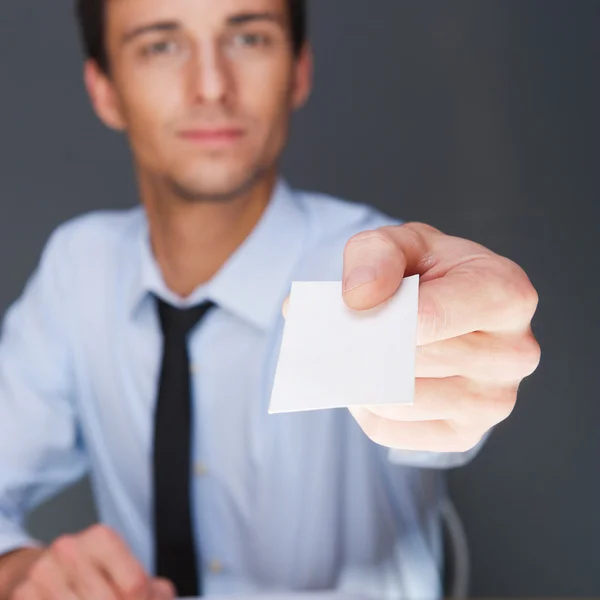 Homem de negócios entregando um cartão de visita em branco sobre fundo cinza — Fotografia de Stock