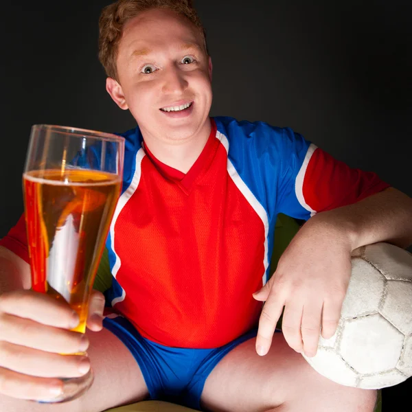 Young man holding soccer ball and beer and watching tv translati — Stock Photo, Image