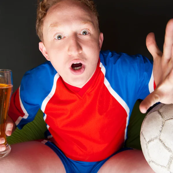 Jovem segurando bola de futebol e cerveja e assistindo TV Translati — Fotografia de Stock