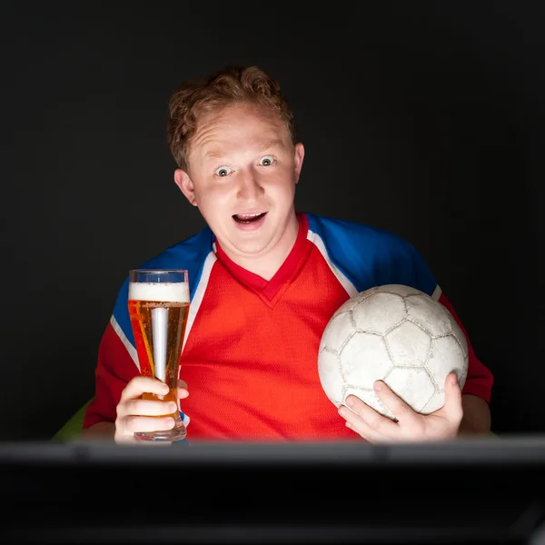 Young man holding soccer ball and beer and watching tv translati Royalty Free Stock Photos