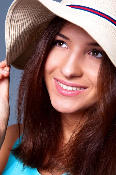 Confident woman with arms near her head holding hat against a blue backgrou — Stock Photo, Image