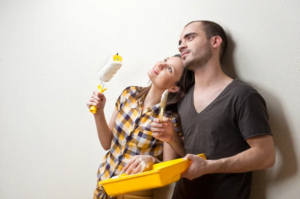 Feliz casal sorrindo pintura parede interior de casa e se divertindo — Fotografia de Stock