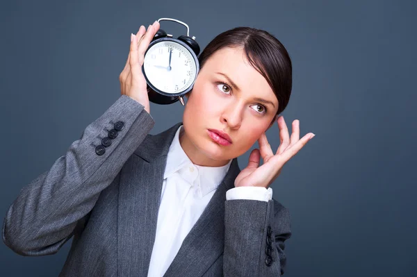 Business woman listening to alarm clock against grey background — Stock Photo, Image