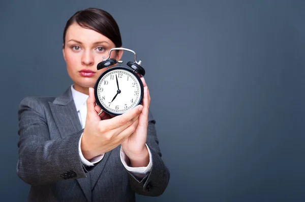 Young business woman showing alarm clock against grey background with copys — Stock Photo, Image